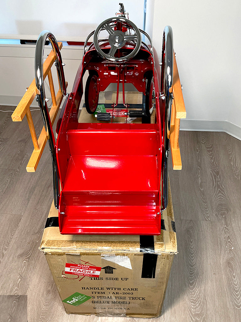 Red toy riding fire engine with its cardboard box 
